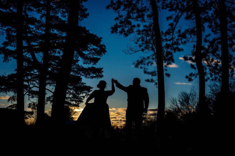silhouette of bride holding dress while being twirled by groom