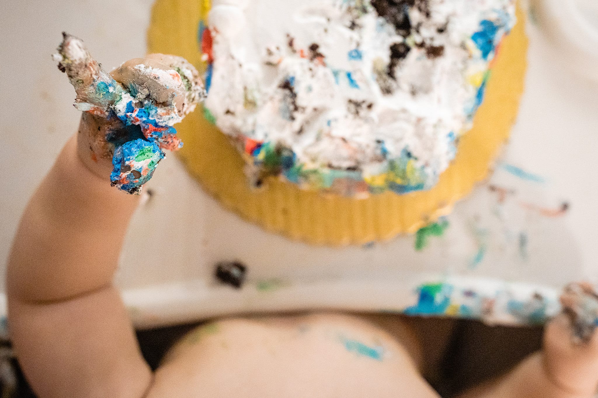 boy sticks up cake-covered fingers during first birthday party