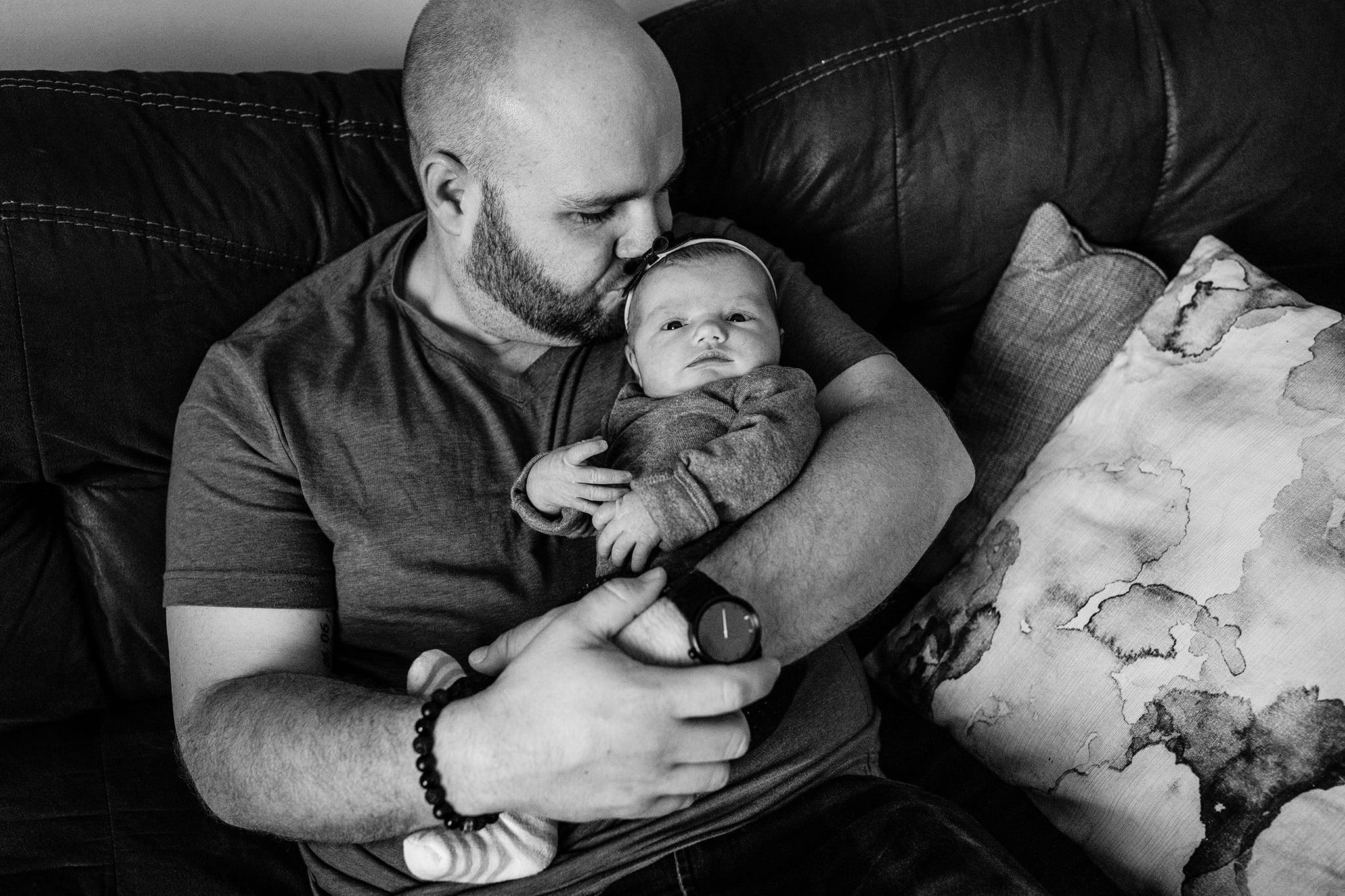 father cuddles newborn at home on couch