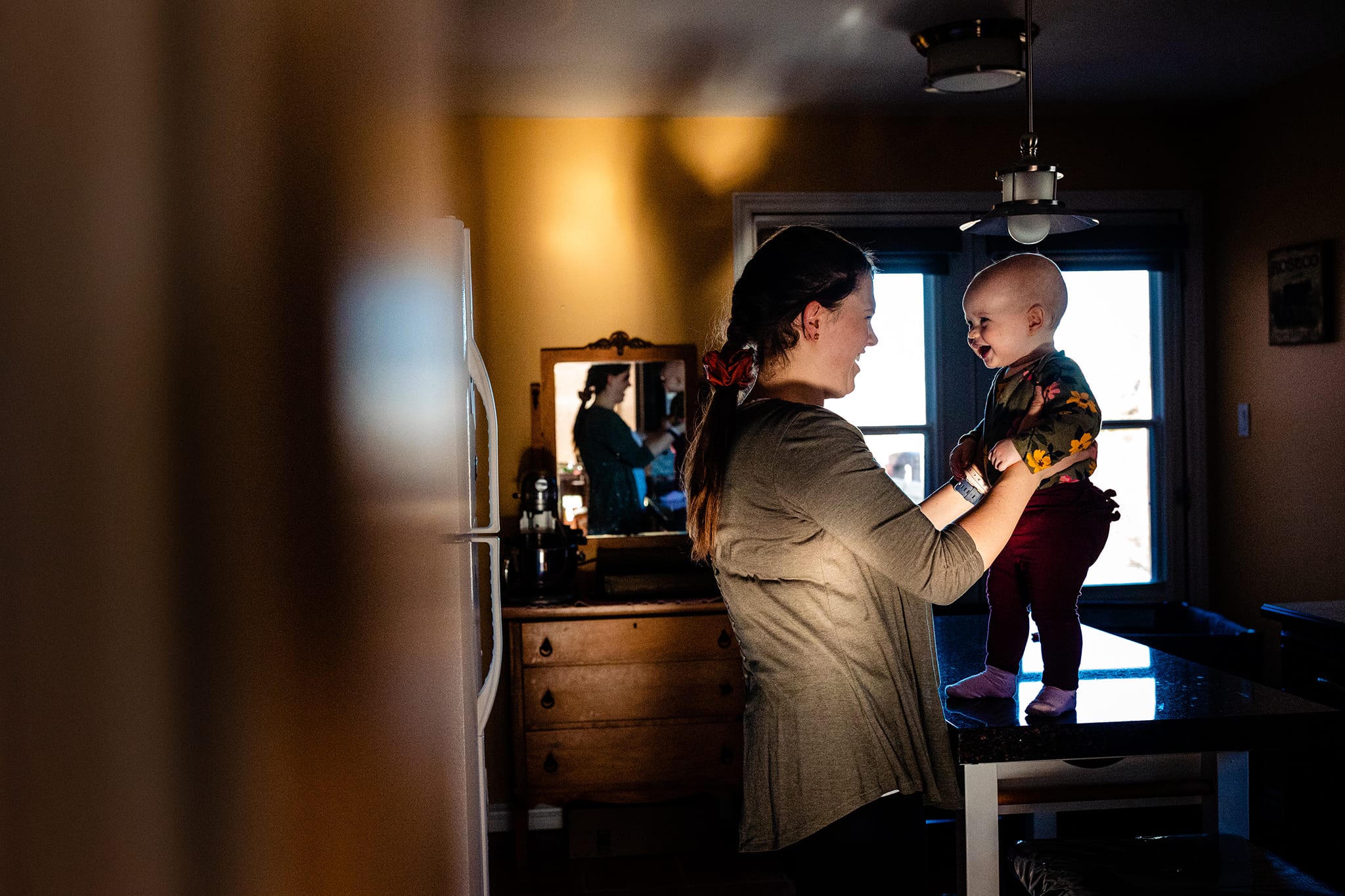 mom holds dancing daughter on counter while lit by afternoon sun