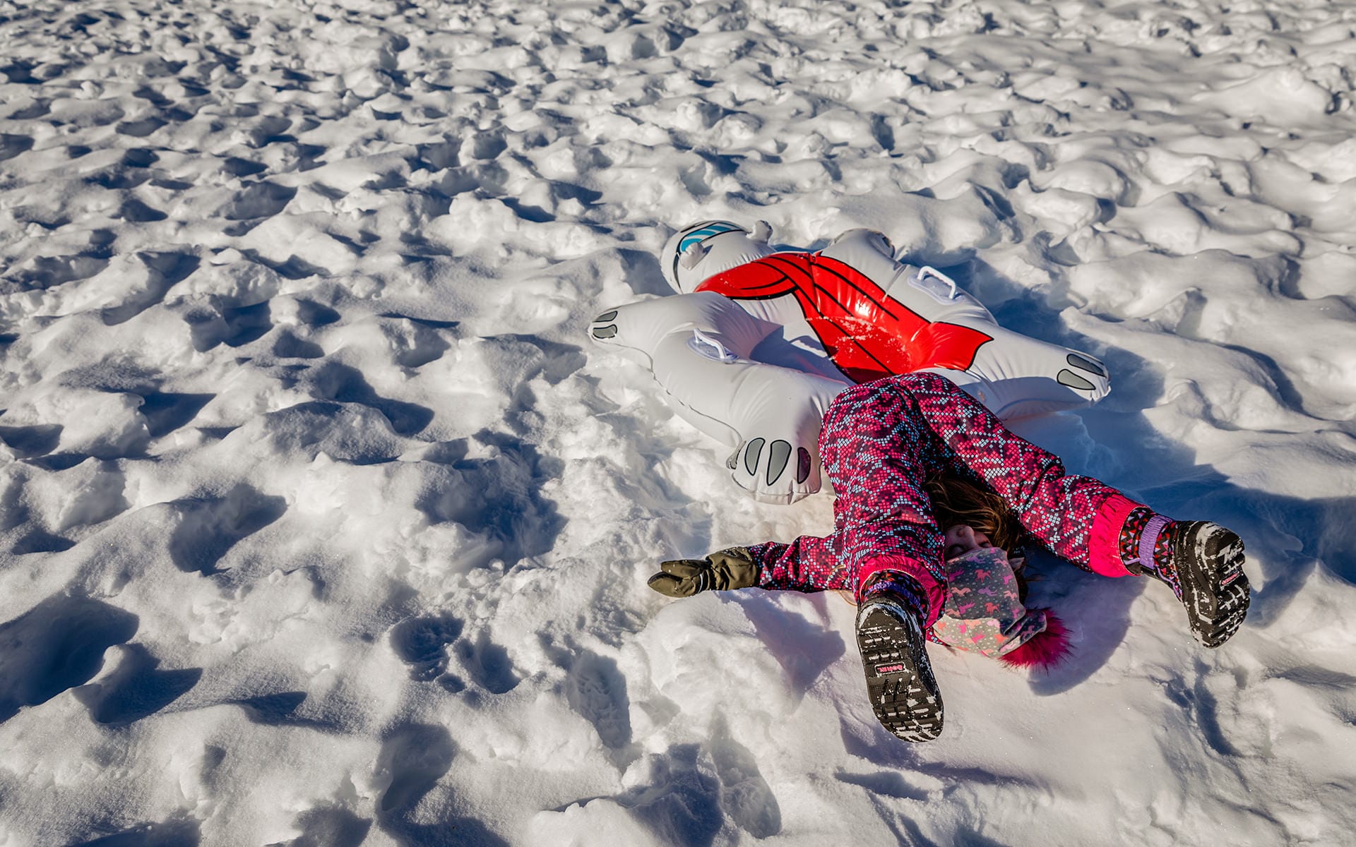 young girl in snow suit lying on snowy ground with feet above head