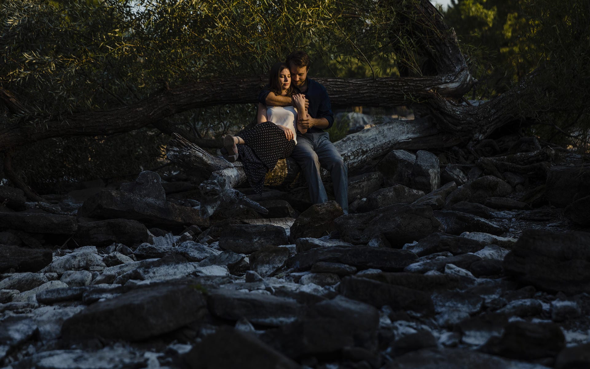 man holds woman closely while sitting on branch in dry riverbed of Ottawa River