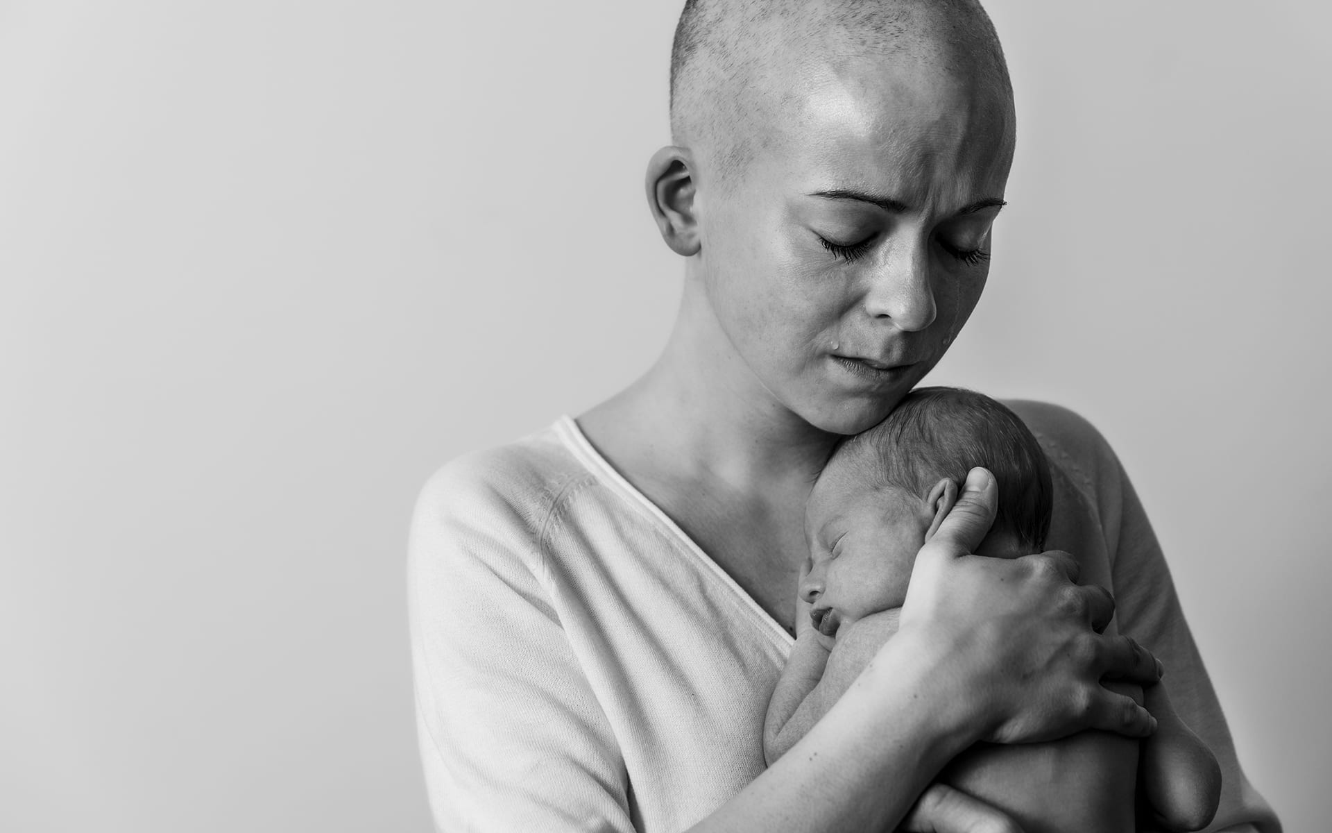 portrait of bald cancer patient crying while holding her newborn