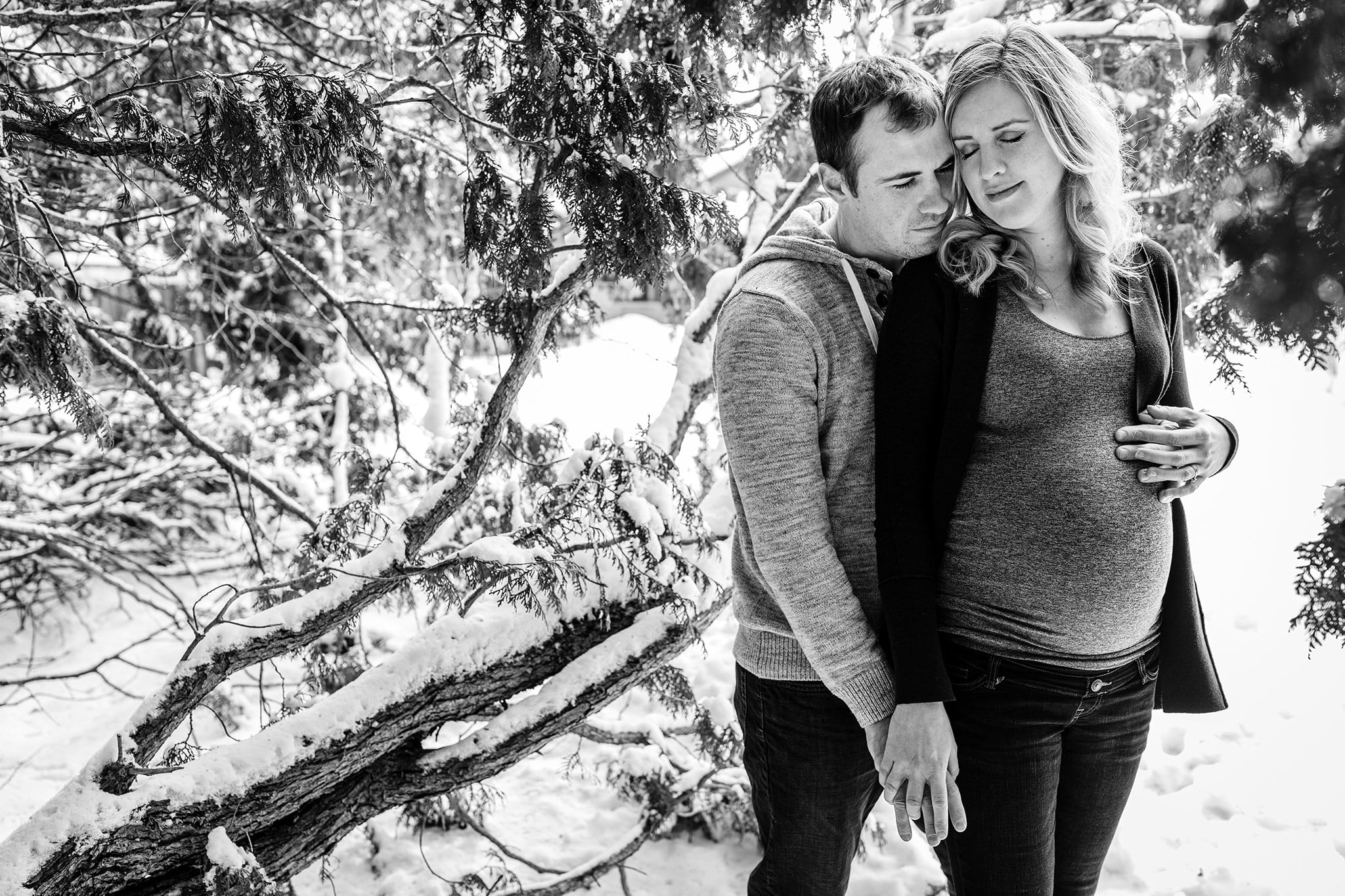 pregnant woman leans against husband surrounded by cedar branches