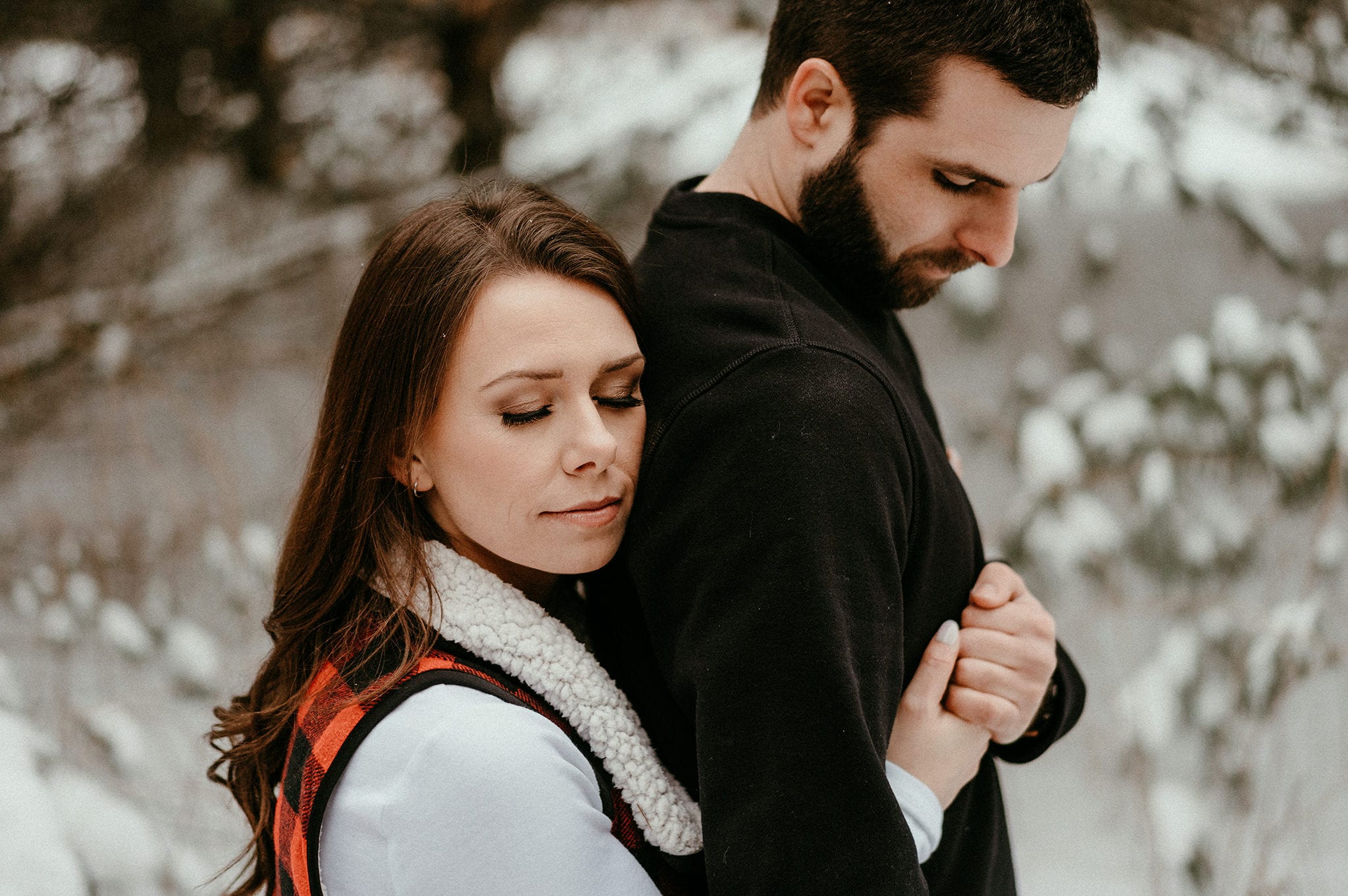 woman hugs fiancé from behind while he holds her hand