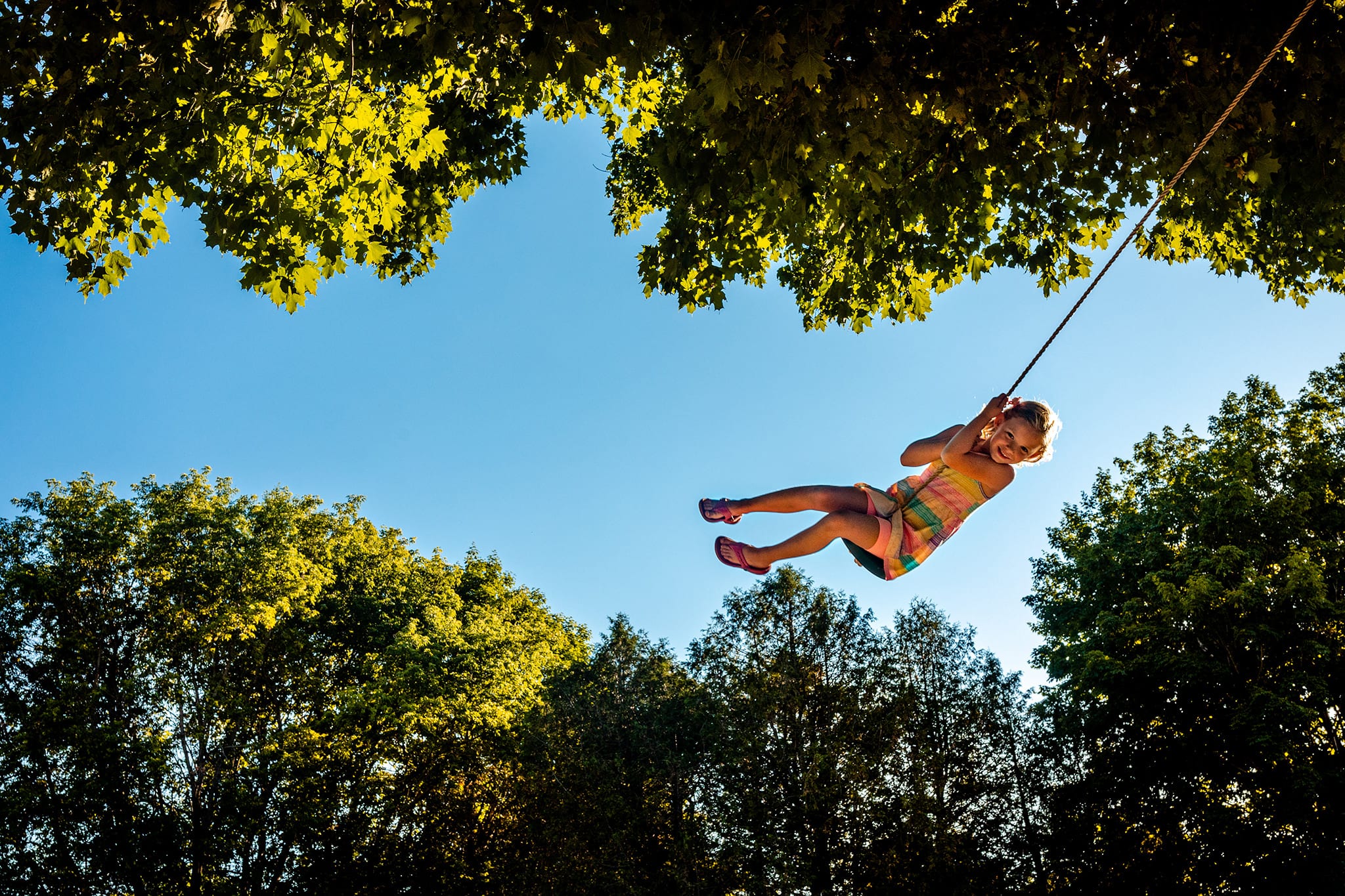girl on tree swing swings into sky between tree branches