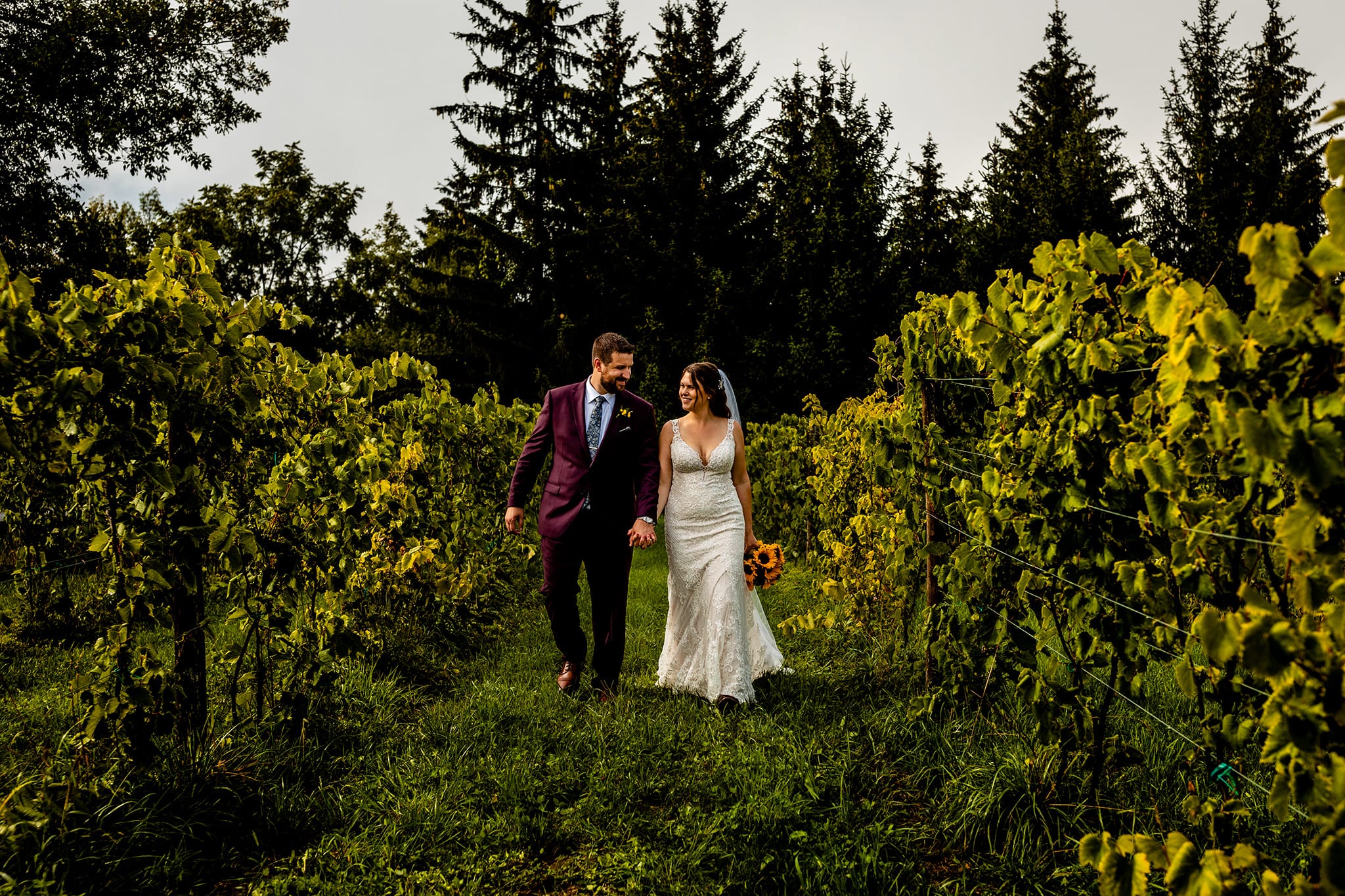 bride and groom hold hands and walk through vines during Summer Stone Crop Acres Wedding