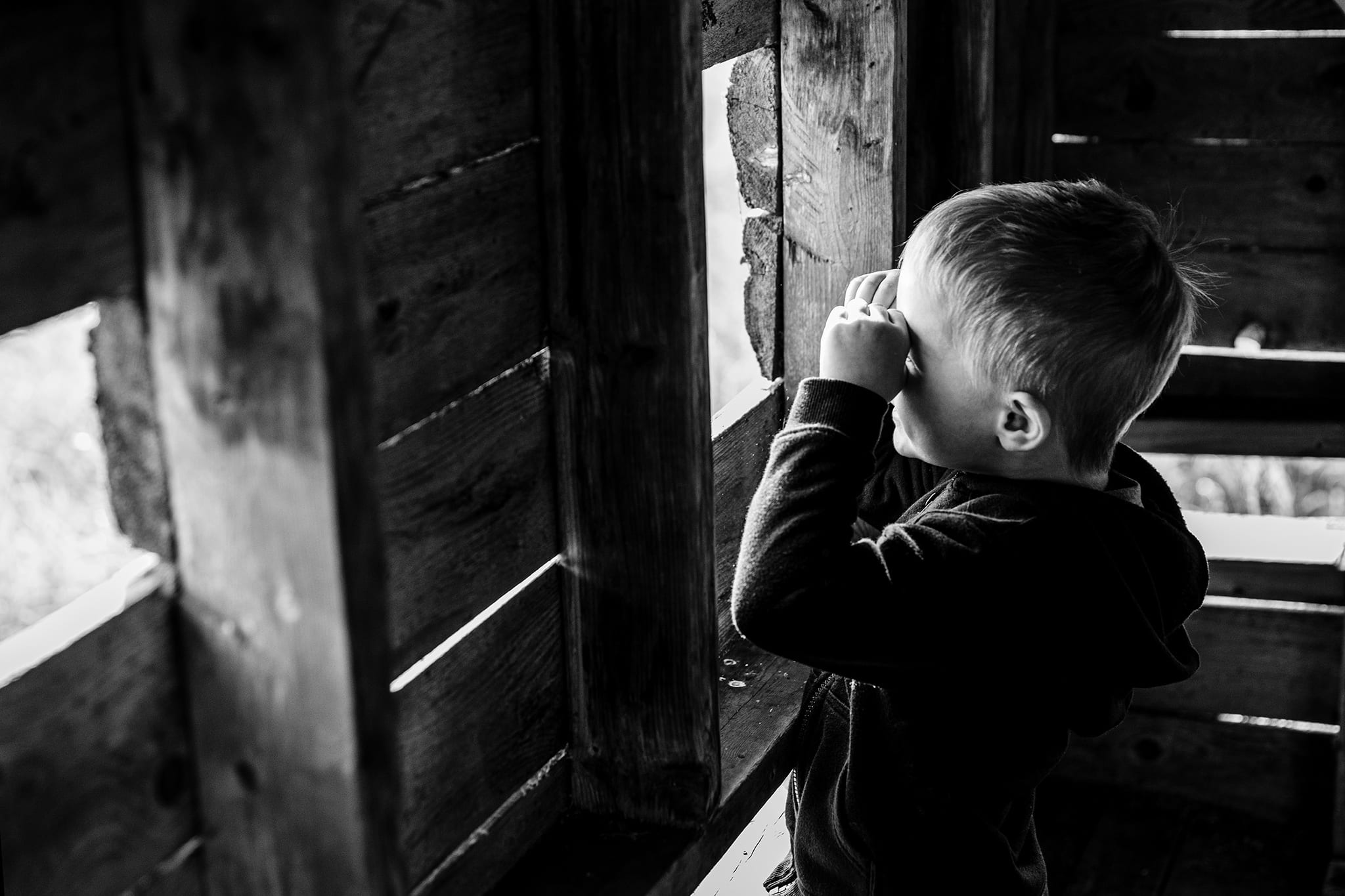 preschool boy in bird blind holds hands up to eyes like binoculars