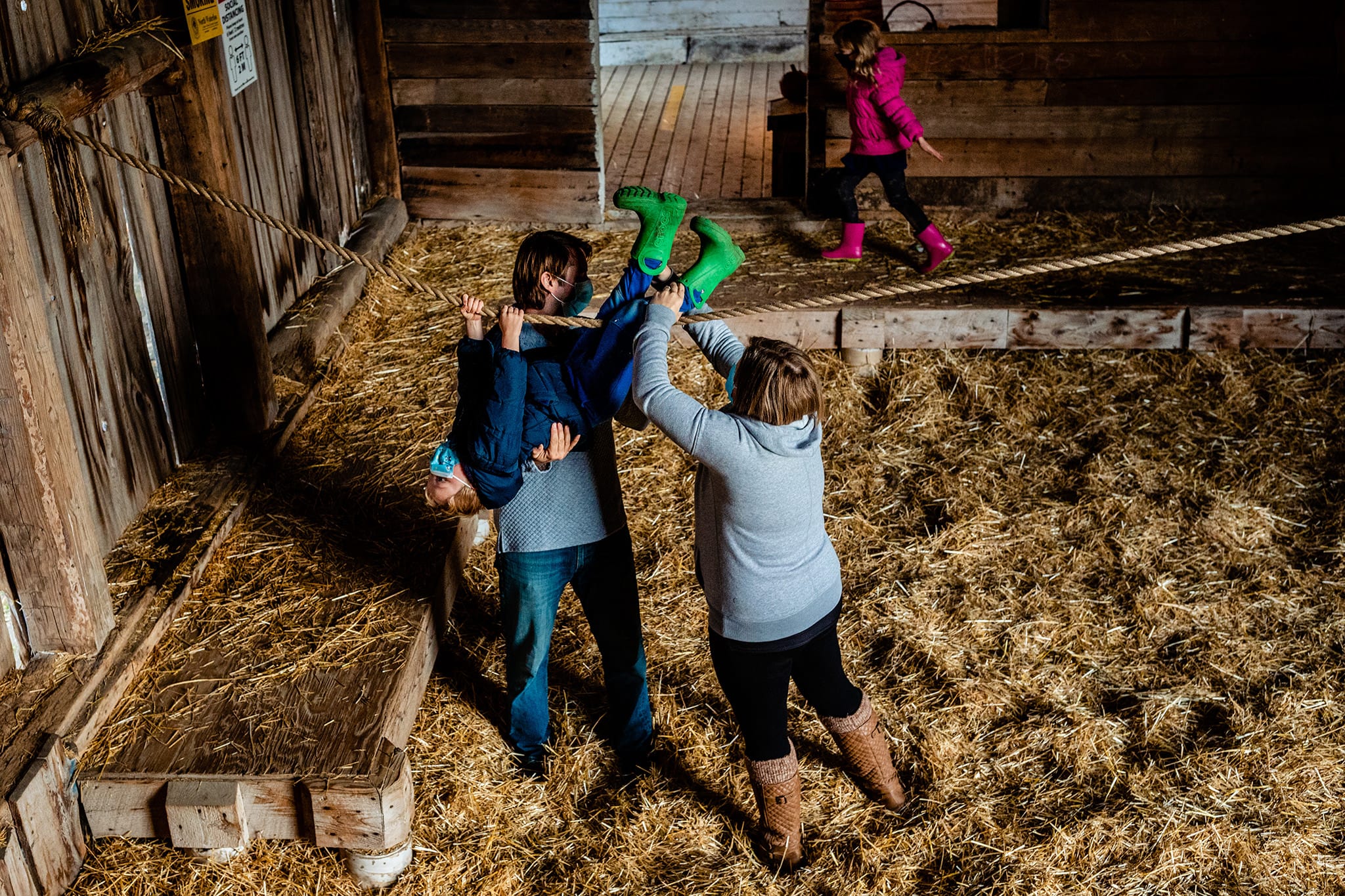 mother and father help son on rope while daughter plays in hay mow