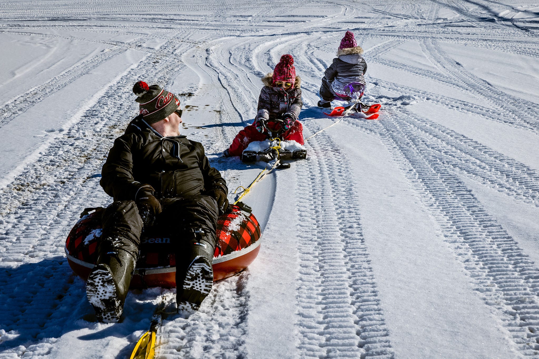 father on tube looks back at two daughters on GT snow racers during Winter Cornwall Documentary Family Photos