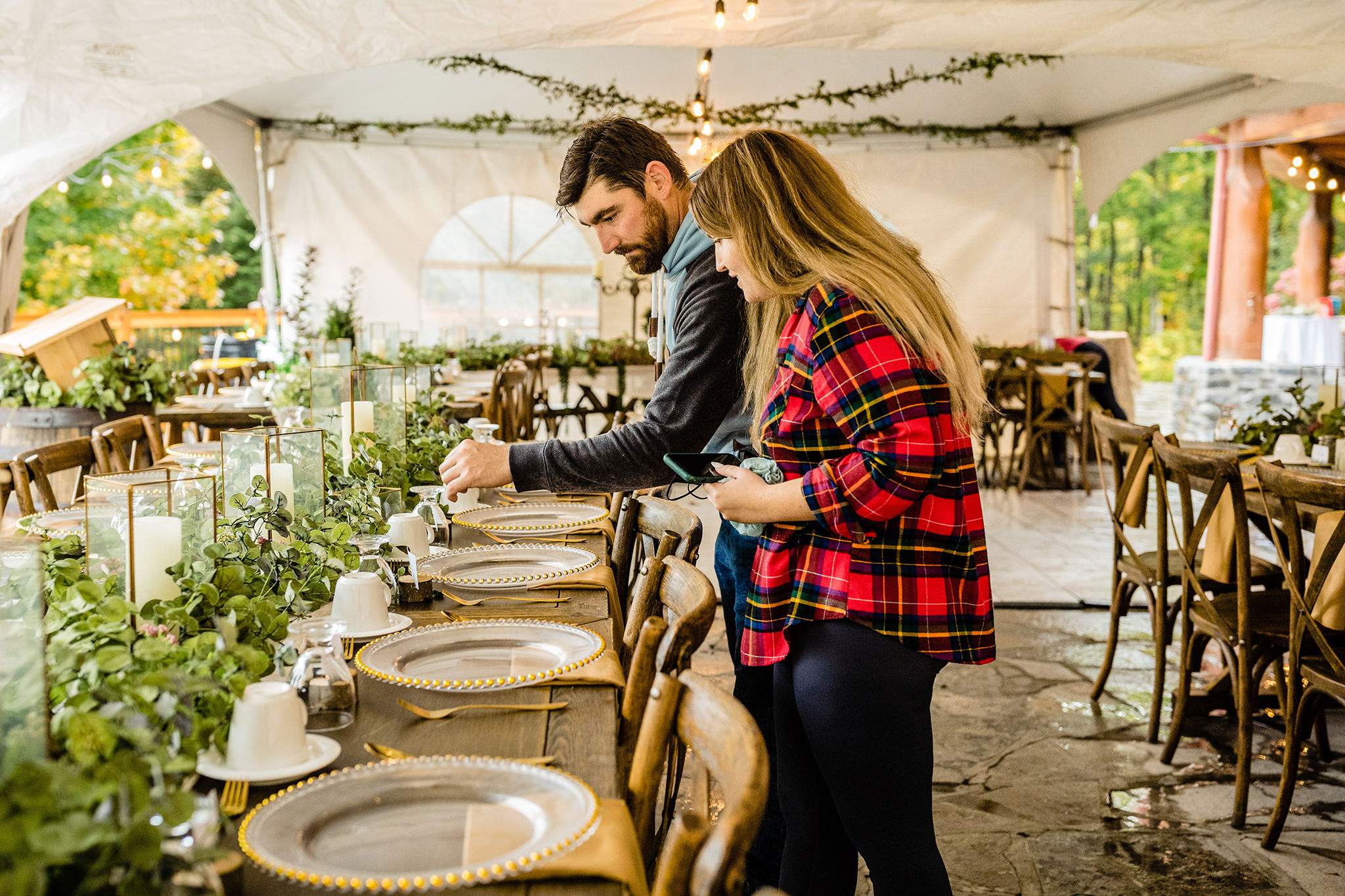 Bride and Groom looking over their wooden reception tables and place settings under a white event tent.