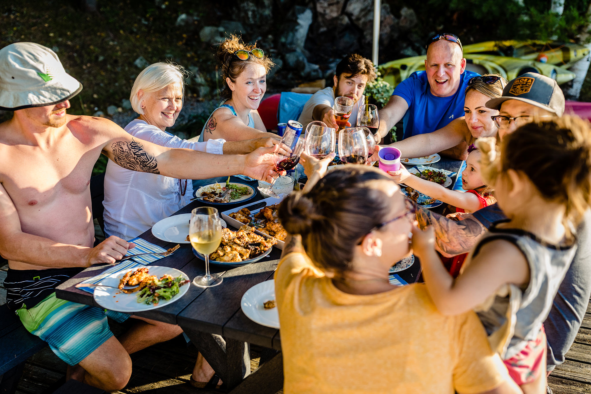 Family smiles while they toast wine and drinks wile enjoying dinner at a picnic table on the dock at Sharbot Lake.
