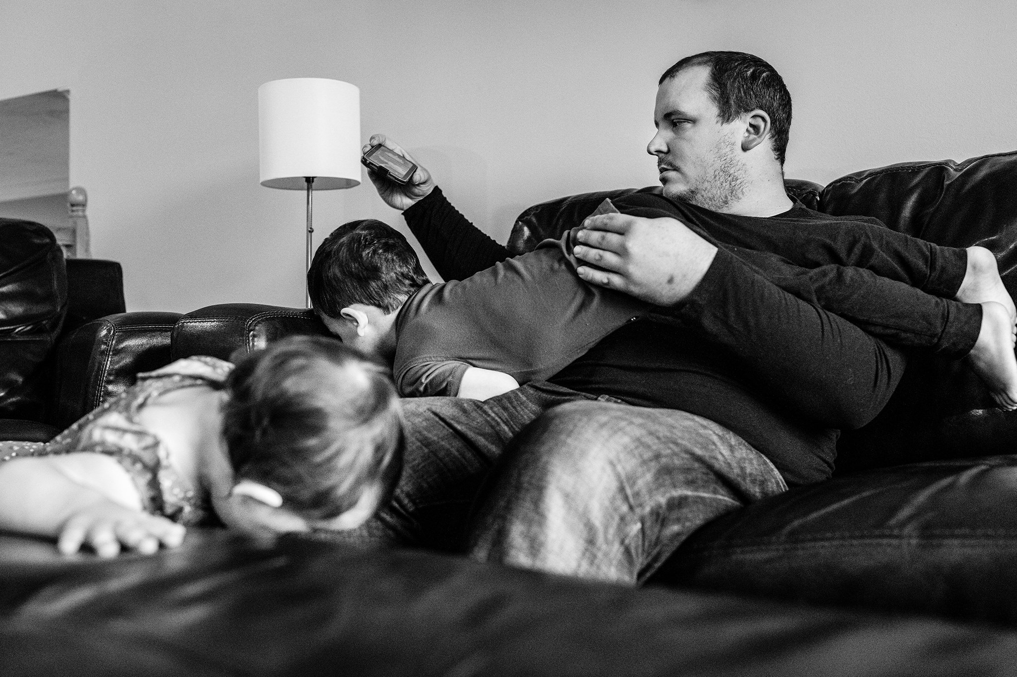 Father watching video on a phone with children playing around and on him