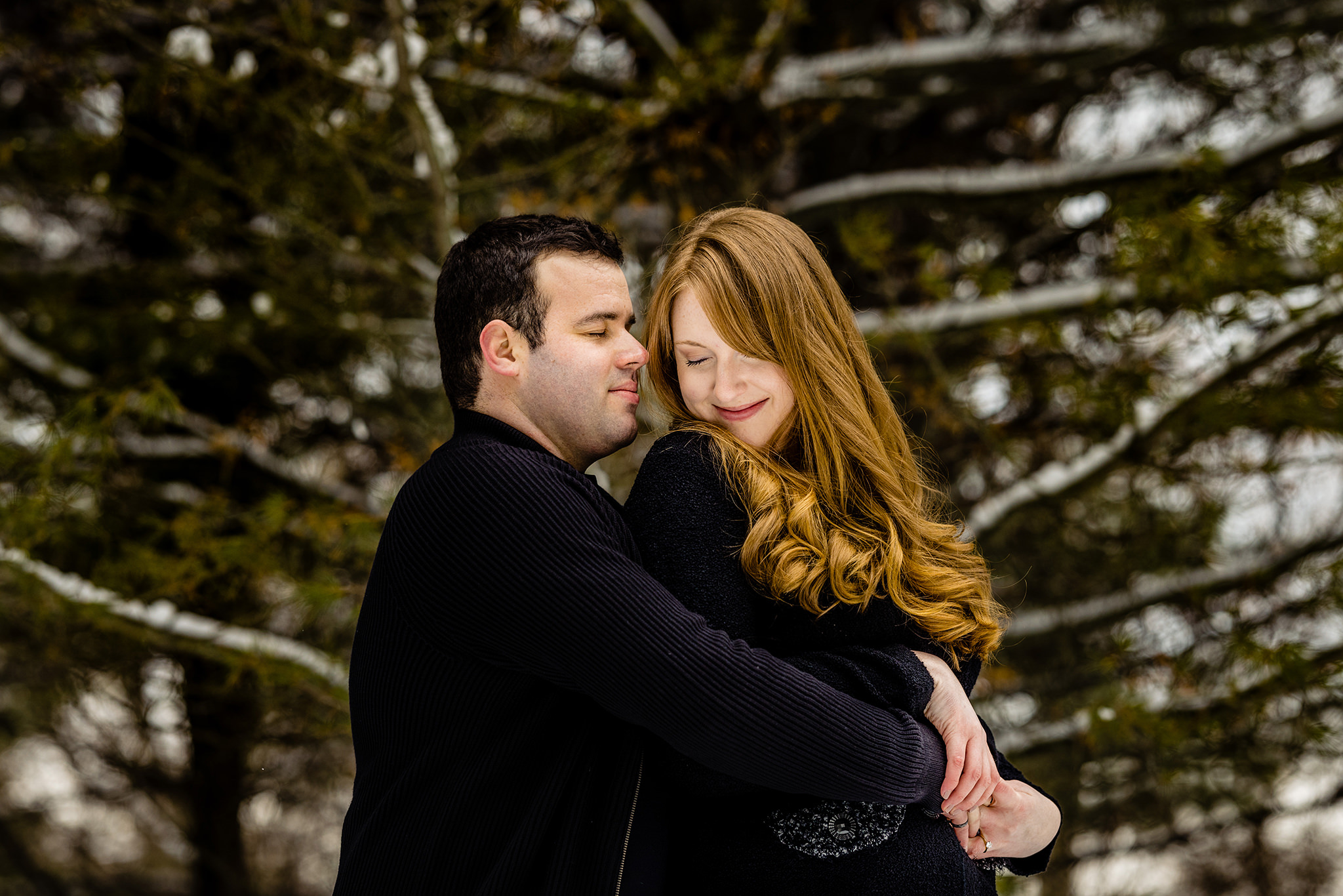 Woman smiling looking back at fiance hugging her in a snowy forest.