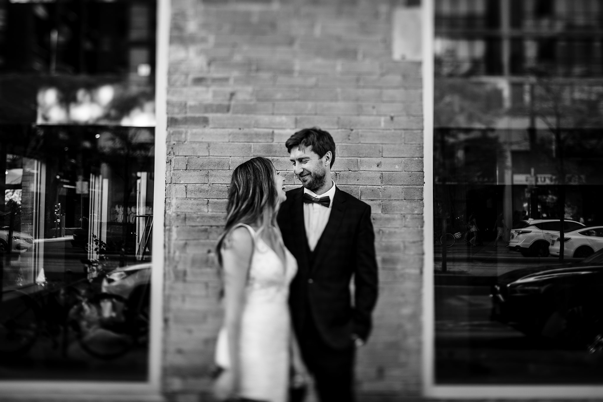 Groom and Bride outdoors in the city laughing in front of a brick wall.