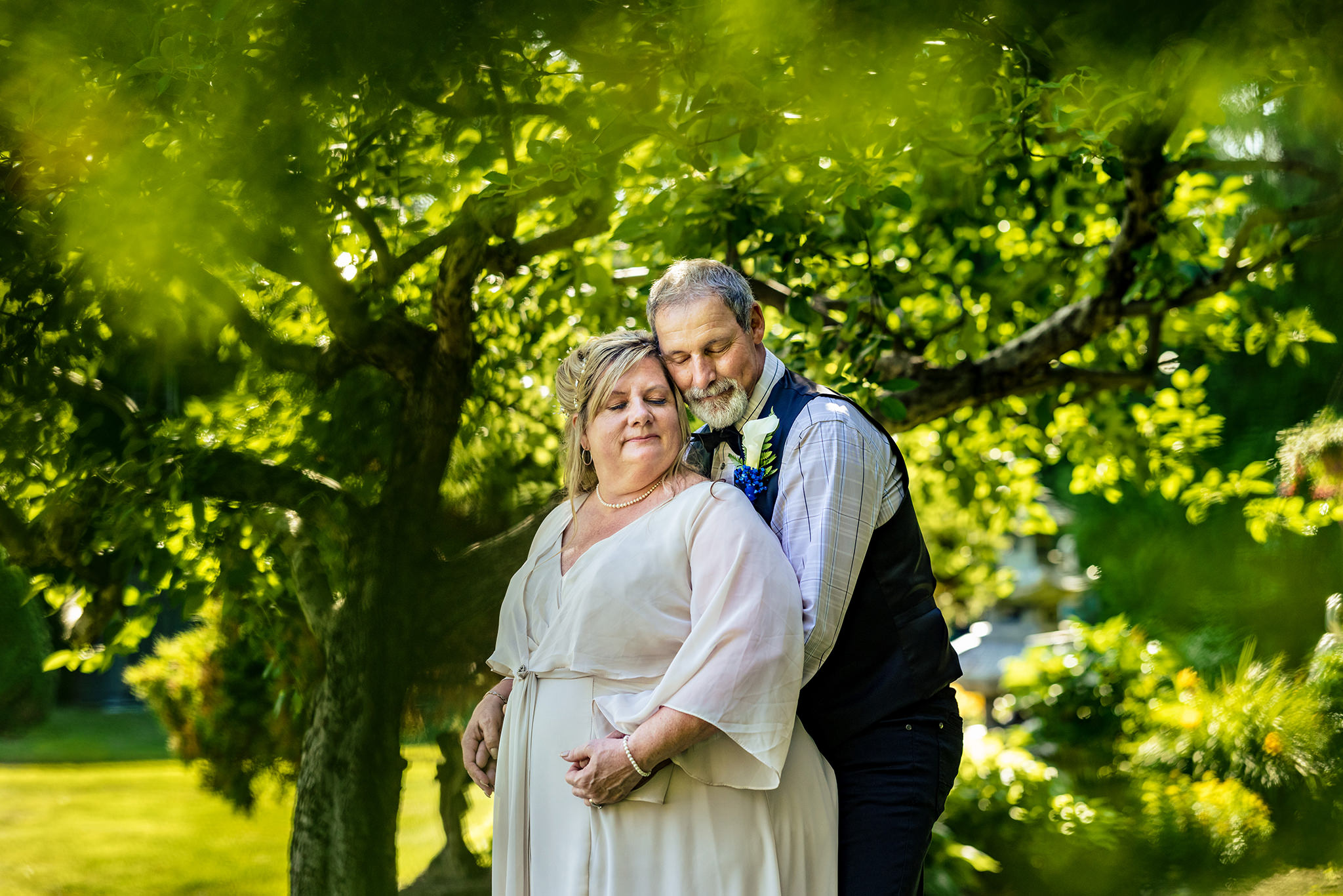 Senior couple embrace spoon-style under apple tree