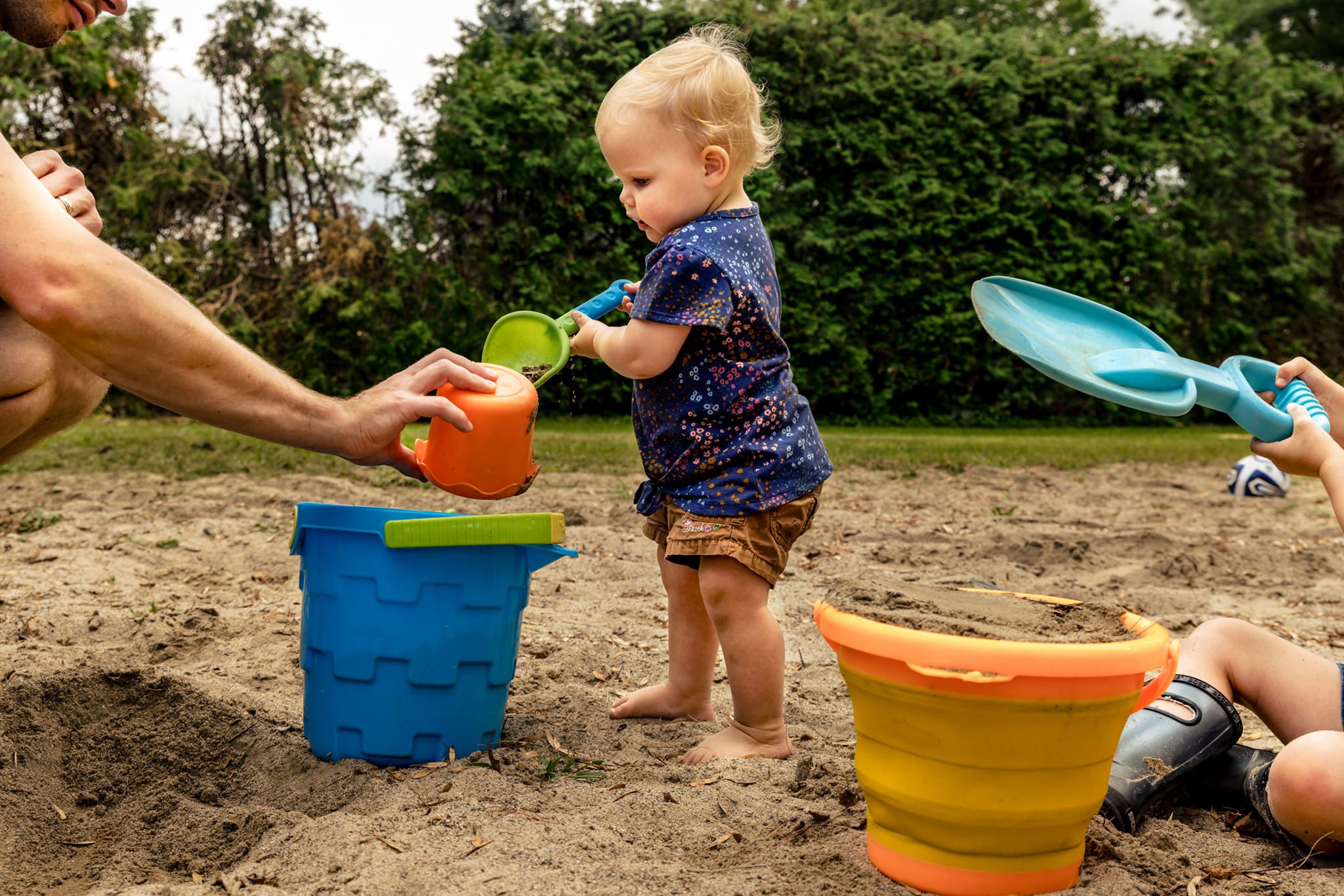 baby scoops sand into bucket held by dad