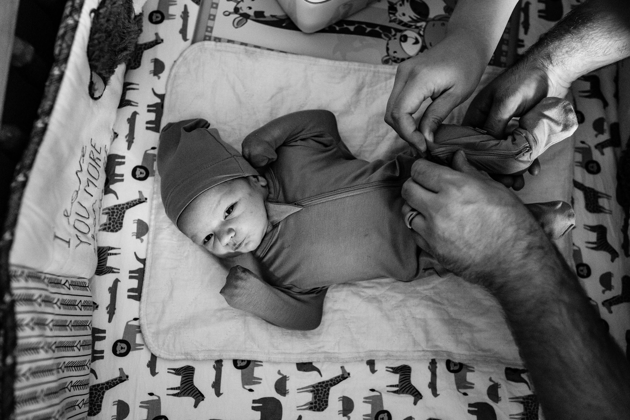 hands reach to fasten snap on baby onesie as newborn boy looks up from crib mat