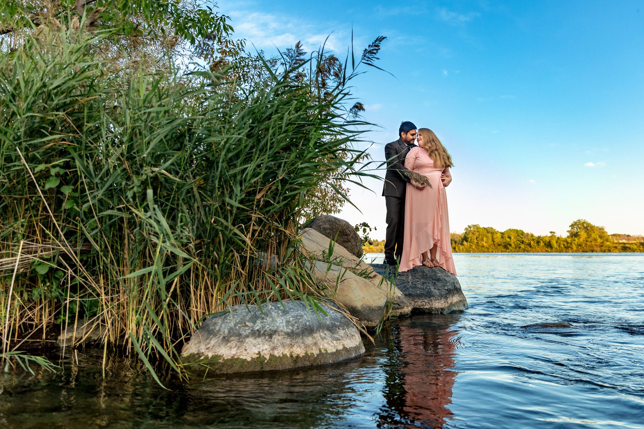 man and woman stand close on rocks beside St Lawrence River in Lamoureux Park