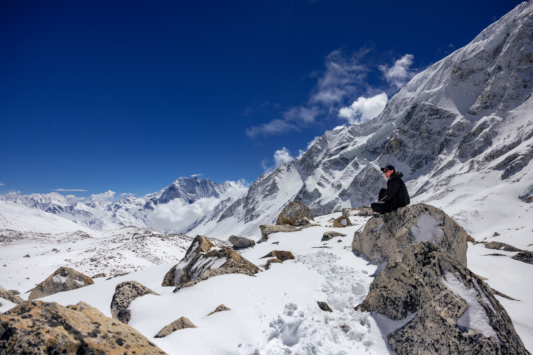 Woman sits on rock on Larkya La Pass in Manaslu Circuit with Himalaya Mountains behind her
